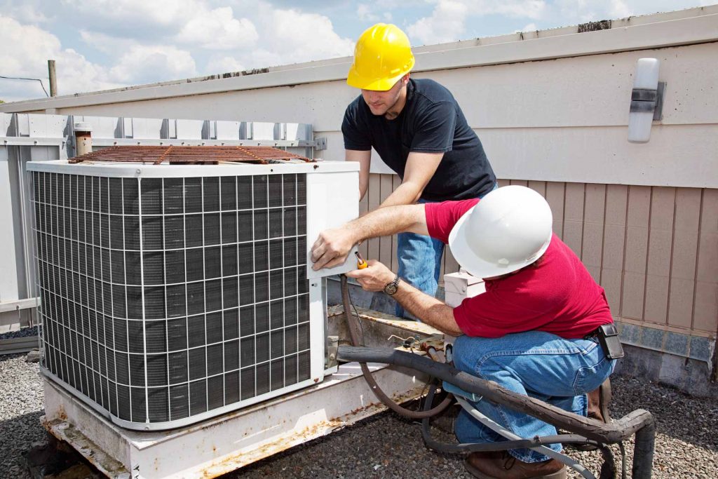Two HVAC technicians working on an AC unit