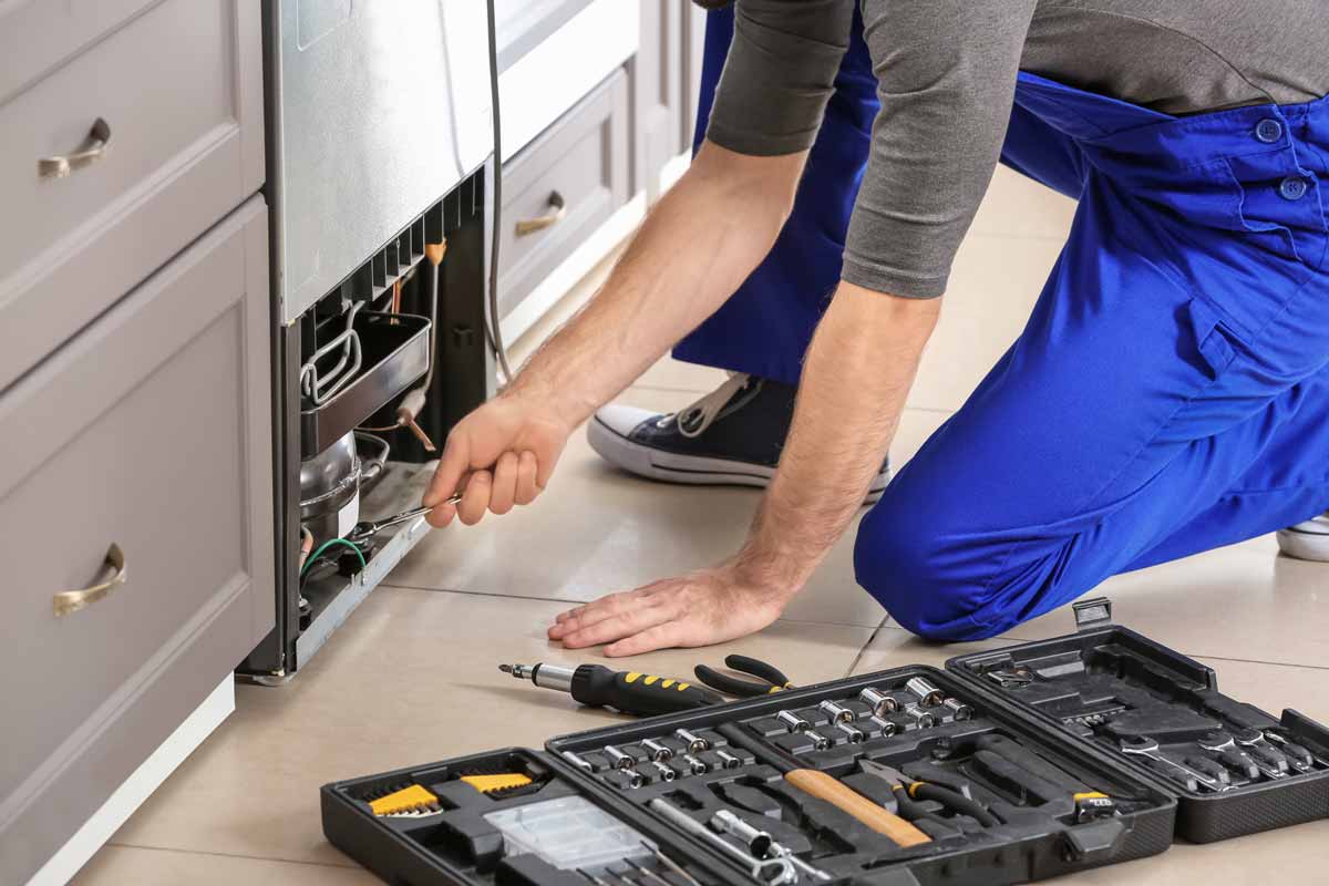 Refrigerator repair technician kneeling to work on a refrigerator